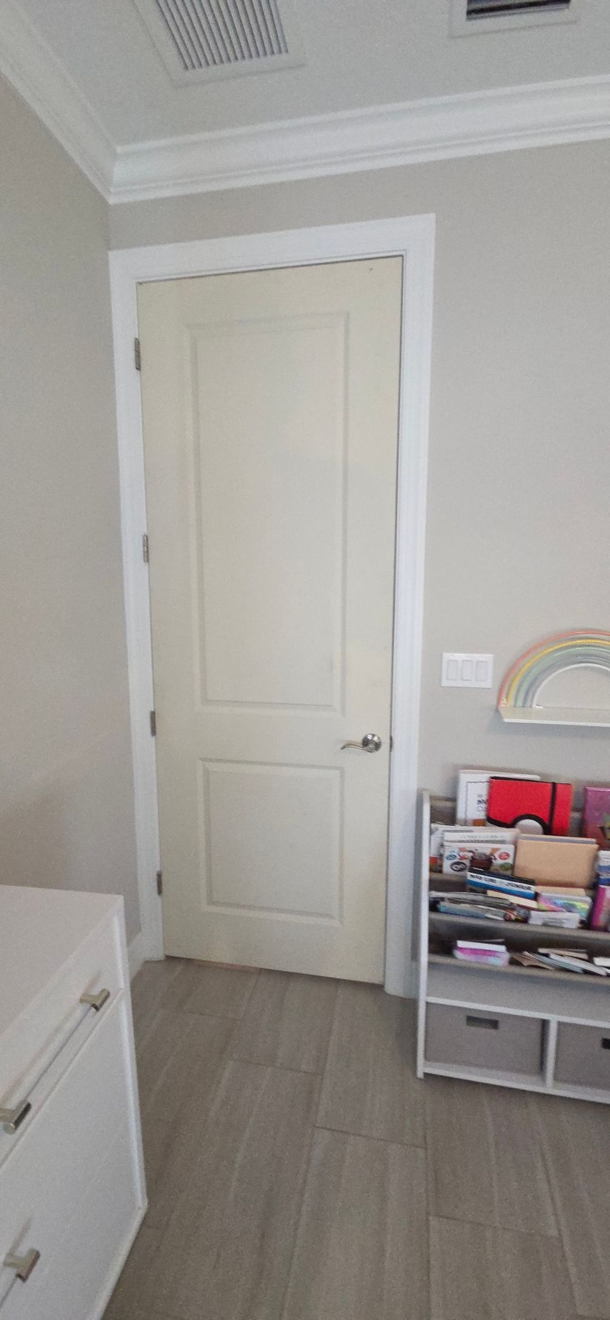 Off-white door with silver handle in a room with light grey walls, white trim and tile flooring.