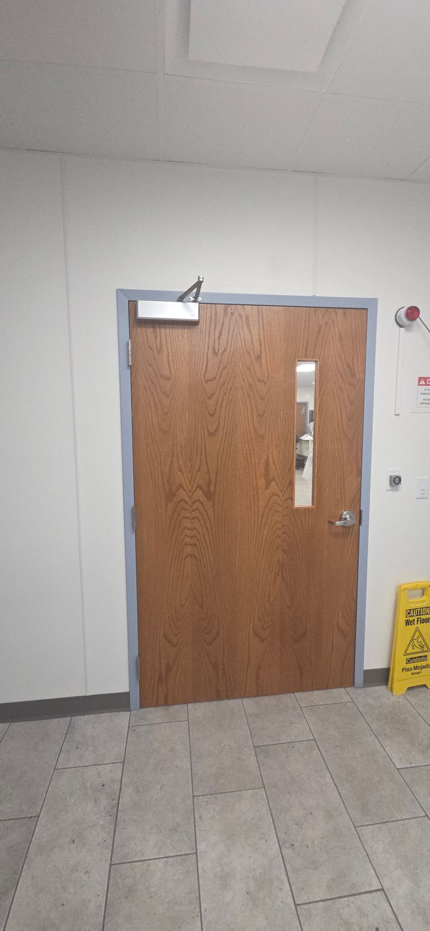 A brown door with a long window and hardware in a room with tiled floors and white walls.