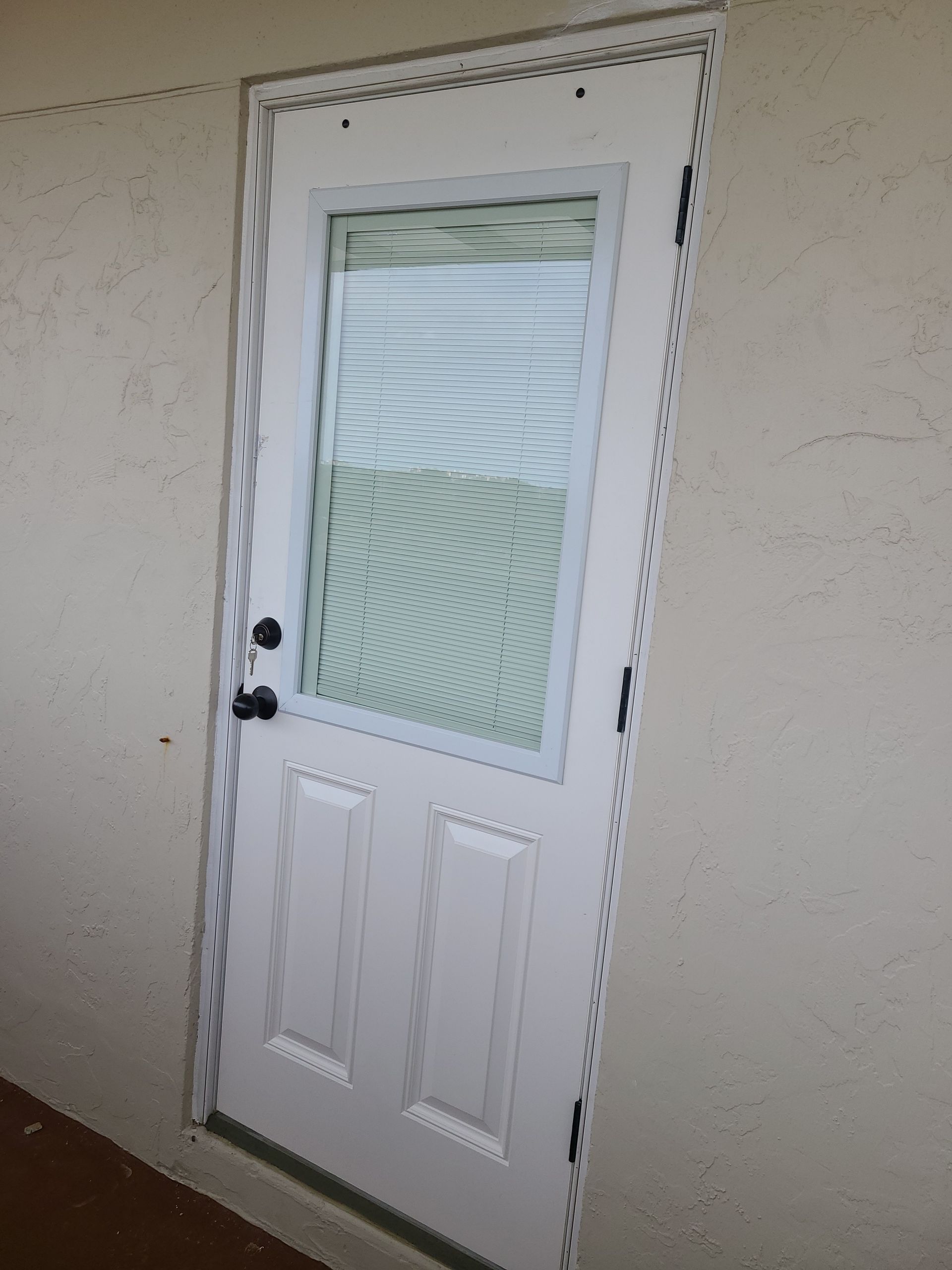 White door with window, black door handle, set into beige wall.