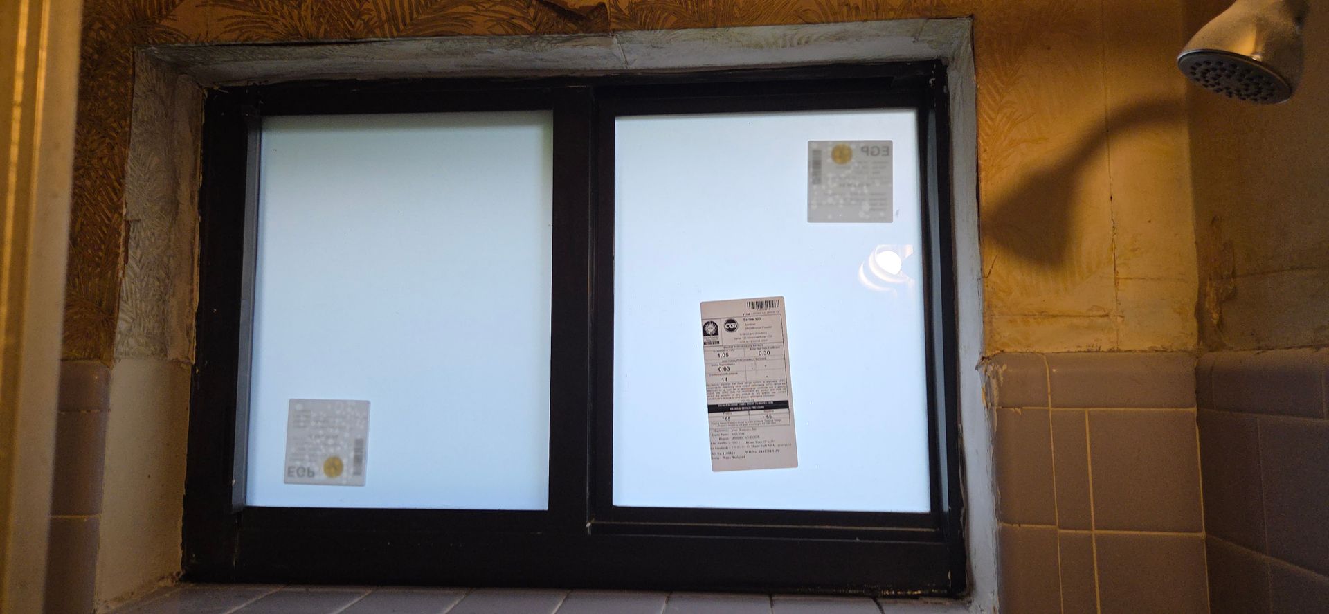 A shower with a frosted window and attached paper. A showerhead hangs from the ceiling.