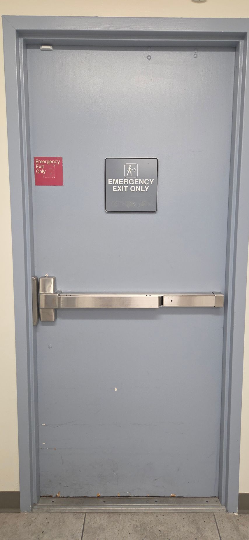 A closed gray door with a push bar, and signs labeled 