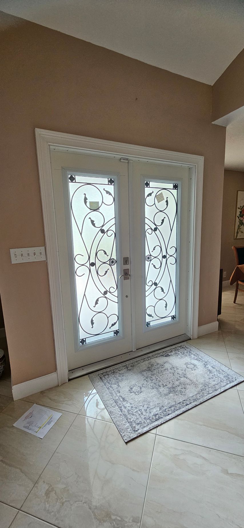 White double doors with frosted glass, floral design, welcome mat, and tiled floor.