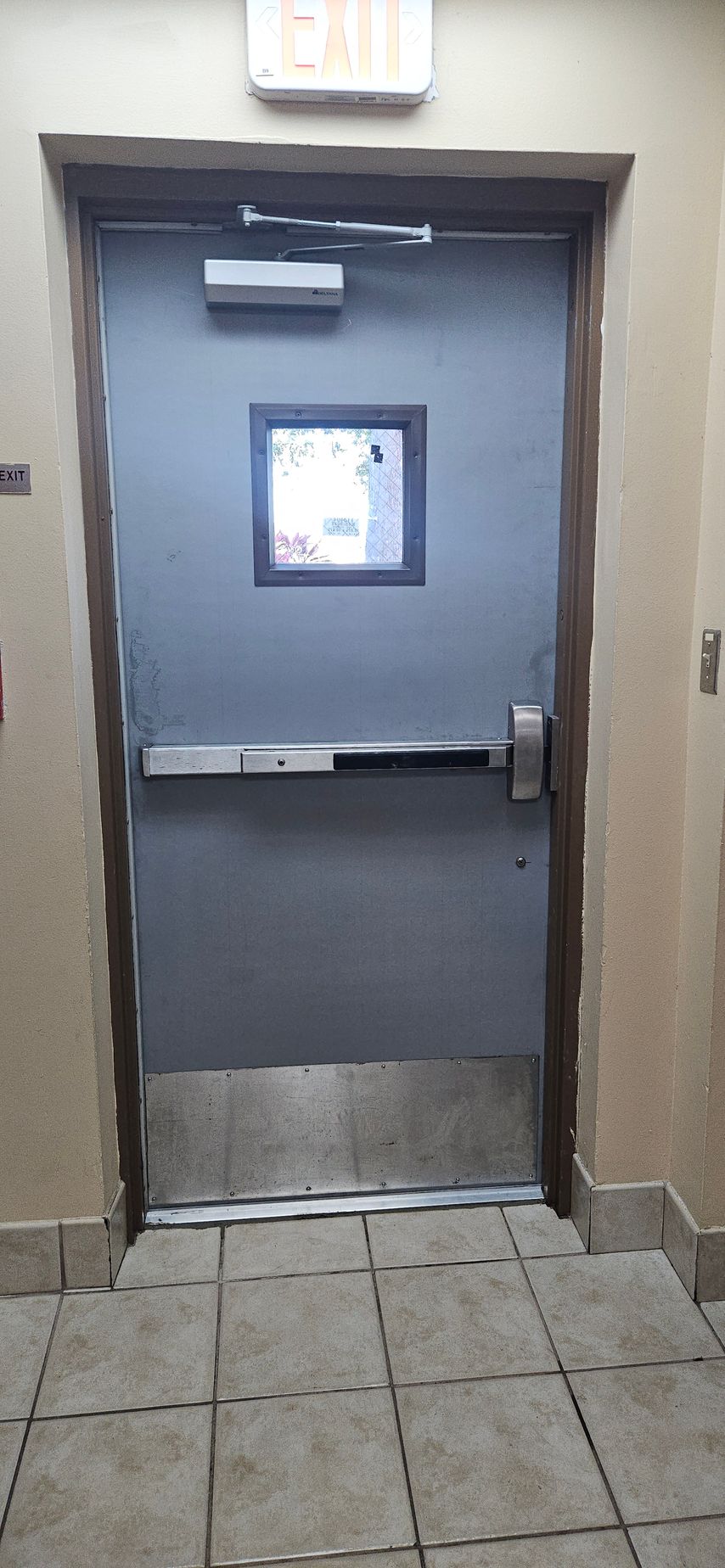 A metal exit door with a push bar, small window, and an 
