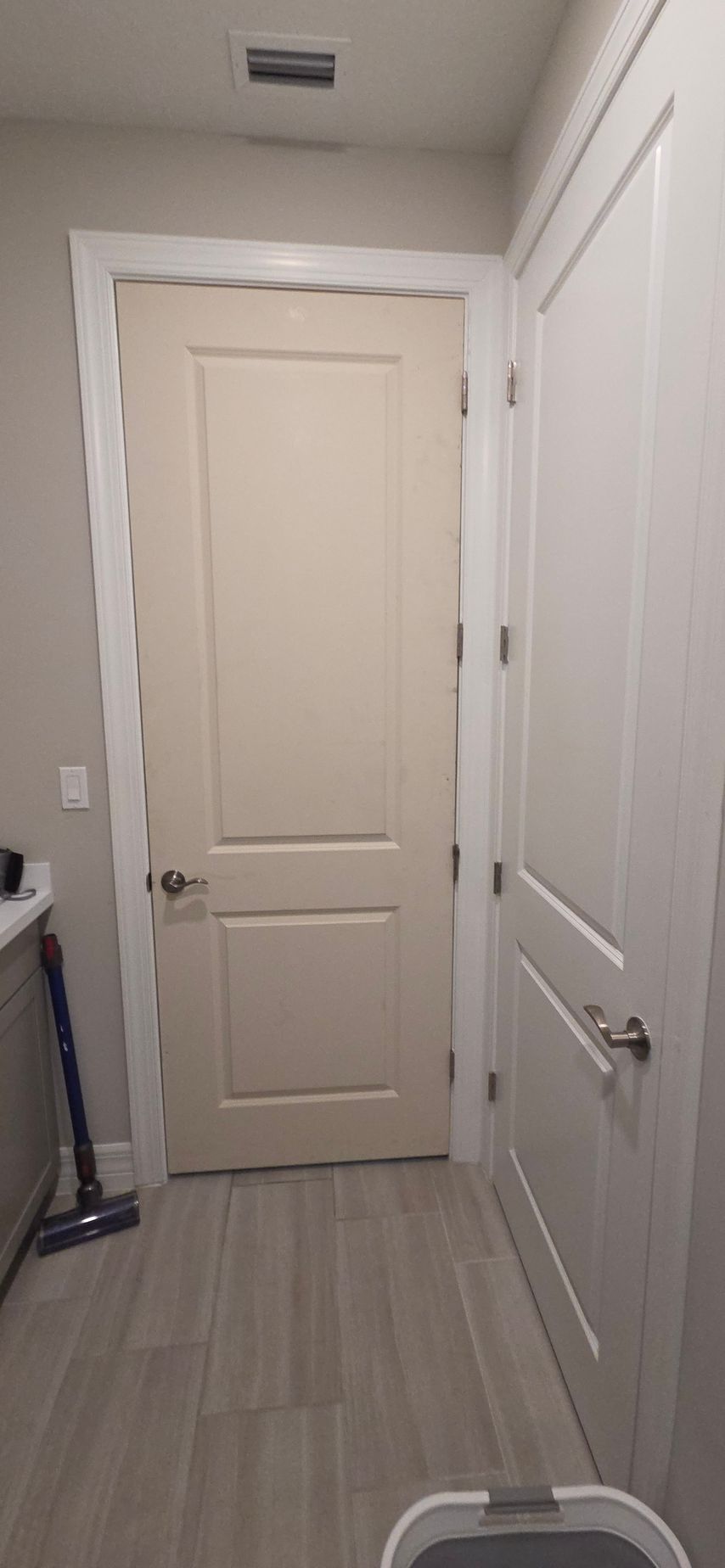 A hallway with two doors and light gray tiled flooring. A vacuum cleaner is in the hallway.