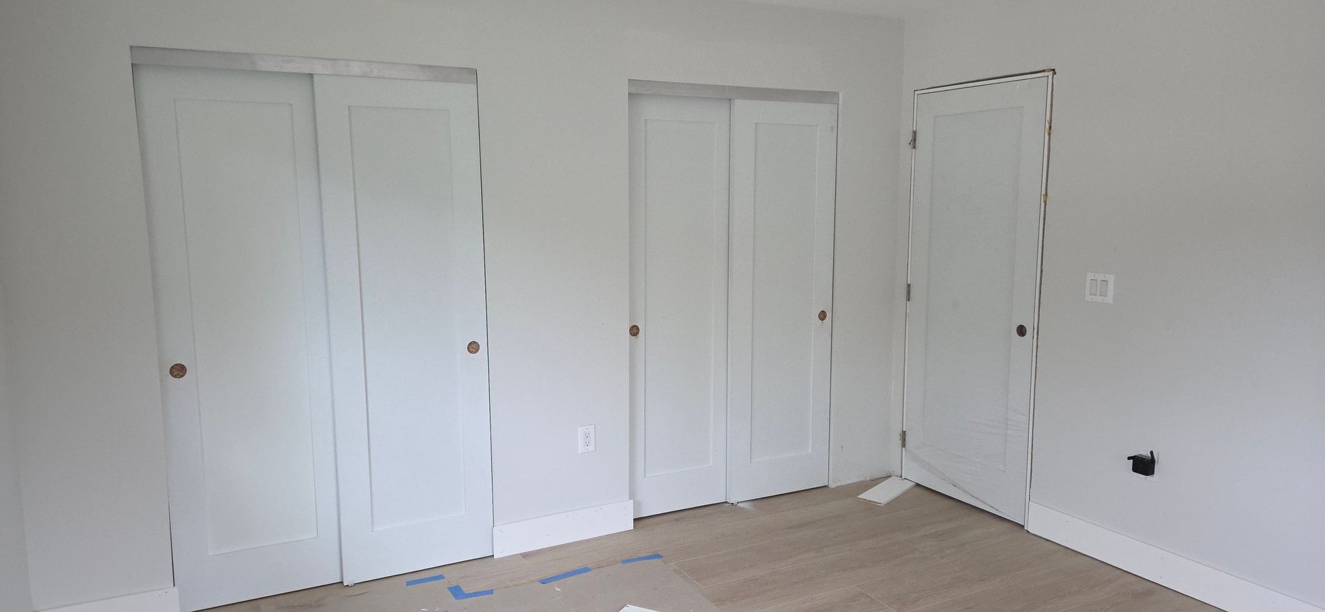 Room with three white doors. Two are sliding closet doors, one is a regular door. Walls and doors are white.