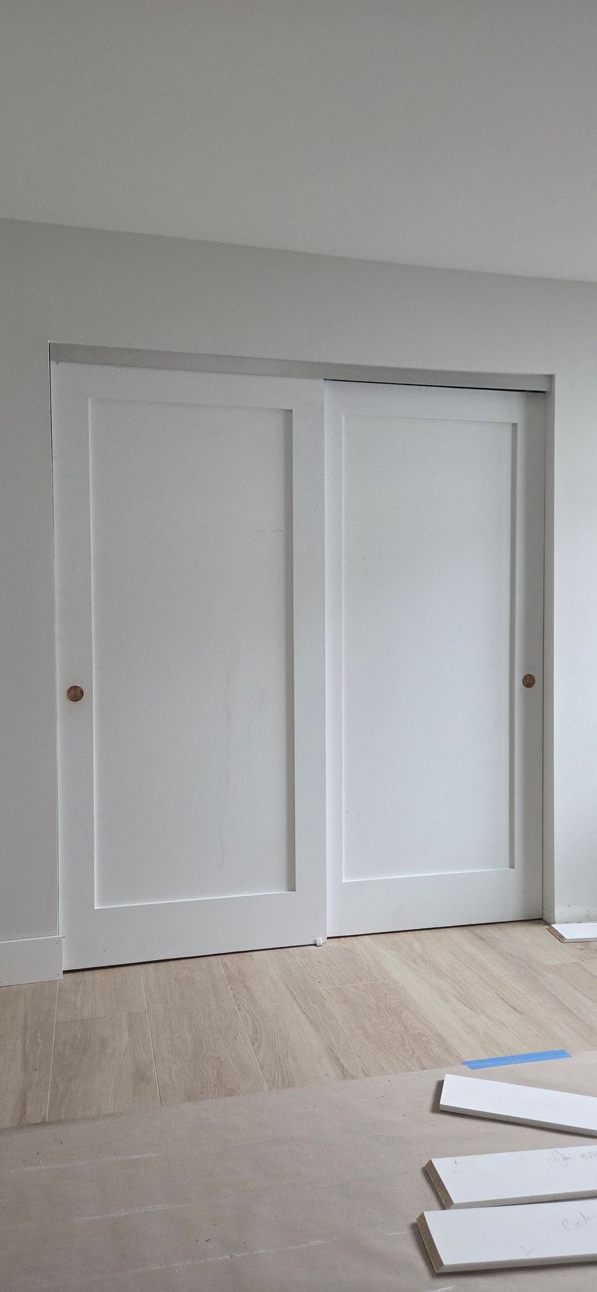 White double sliding doors in a room with light wood floors. Construction materials are in the foreground.