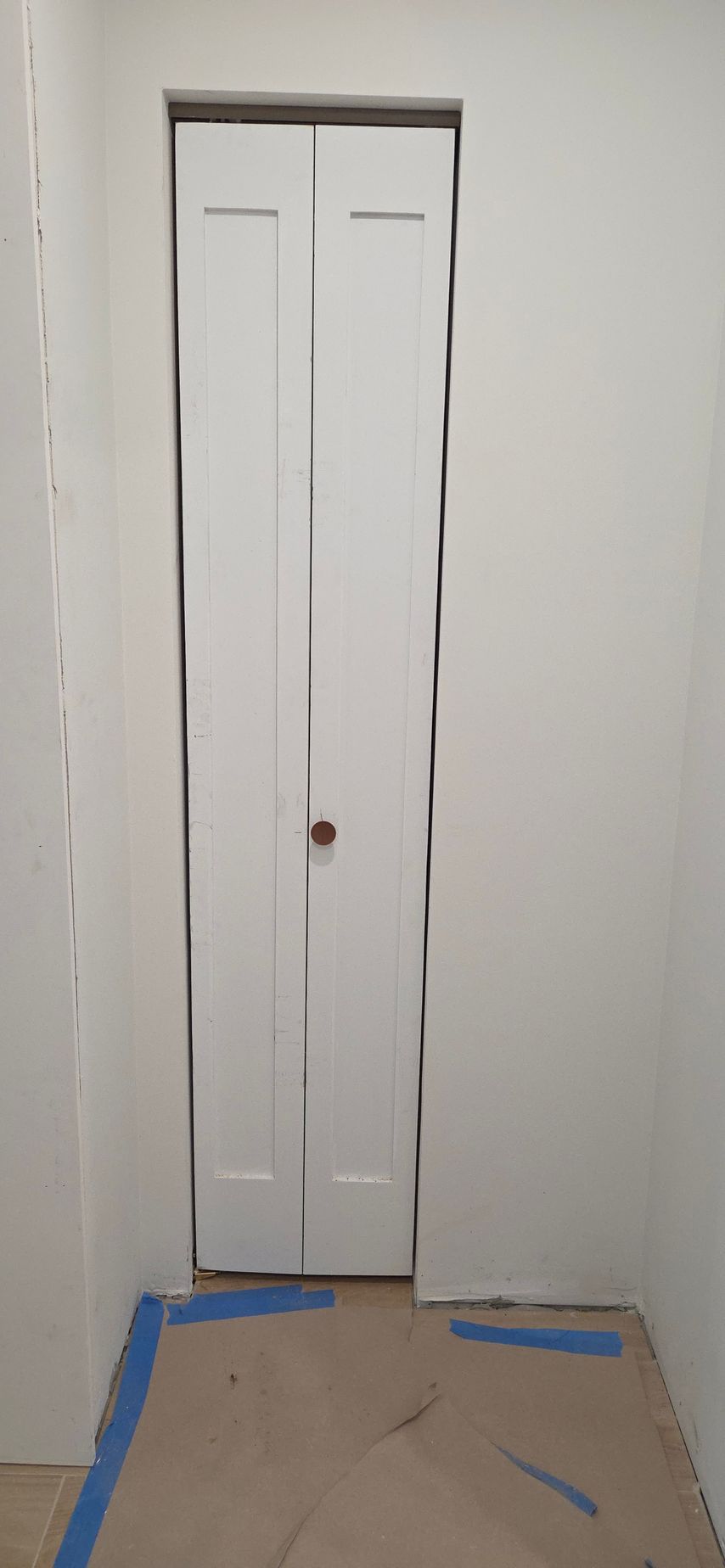 White bi-fold door in a narrow hallway. Floor covered with cardboard and blue tape.