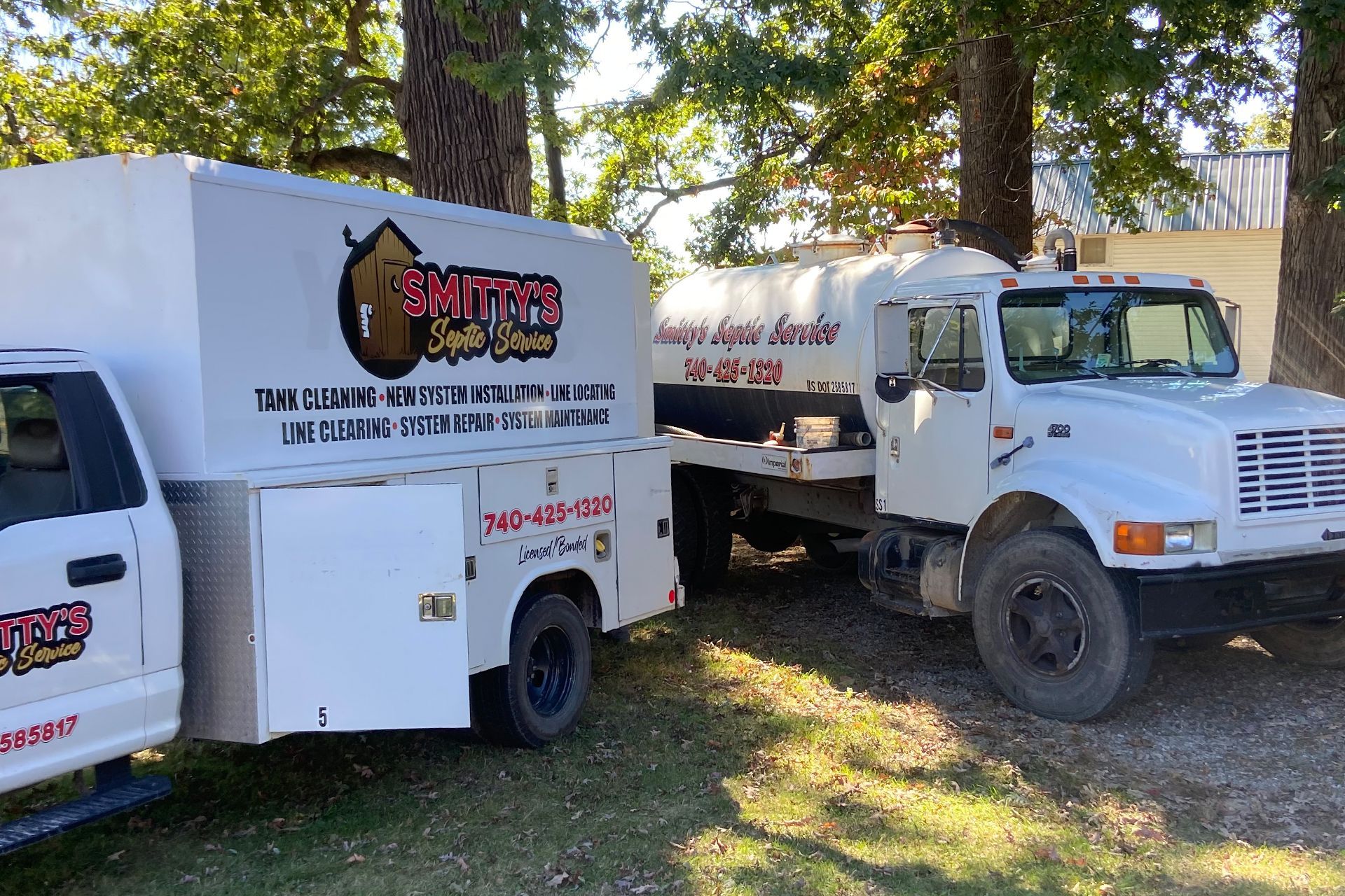Two white service trucks parked outdoors with company logos and phone numbers.
