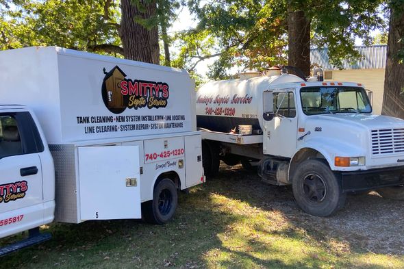 Two white service trucks parked outdoors with company logos and phone numbers.
