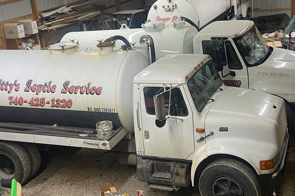 White septic service trucks parked in a barn with business name