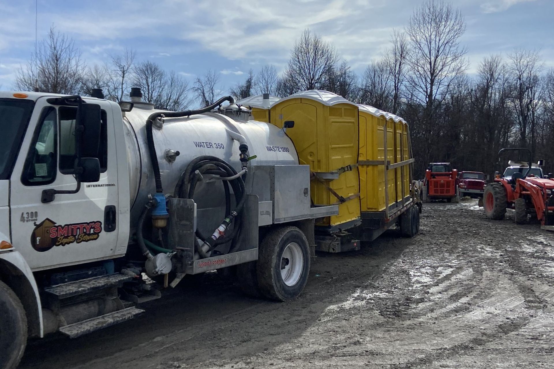 White truck hauling yellow portable toilets on a muddy construction site.
