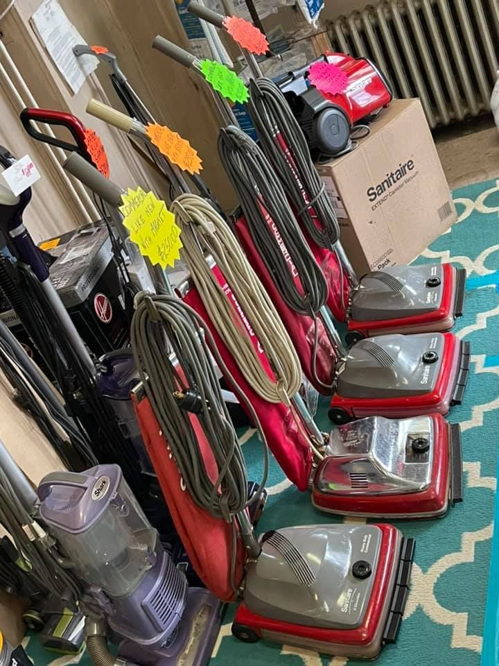 A variety of vacuum cleaners are lined up on a rug in a store