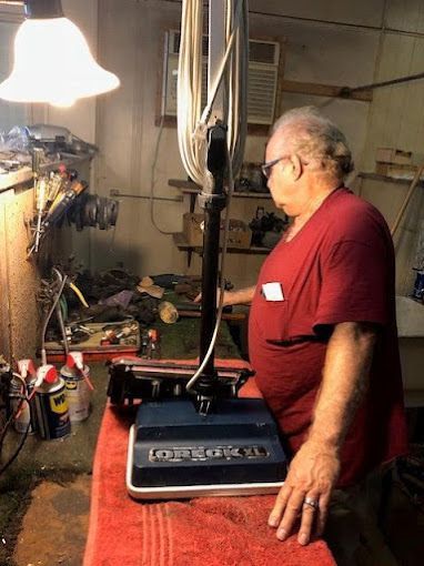 A man in a red shirt is standing next to a vacuum cleaner