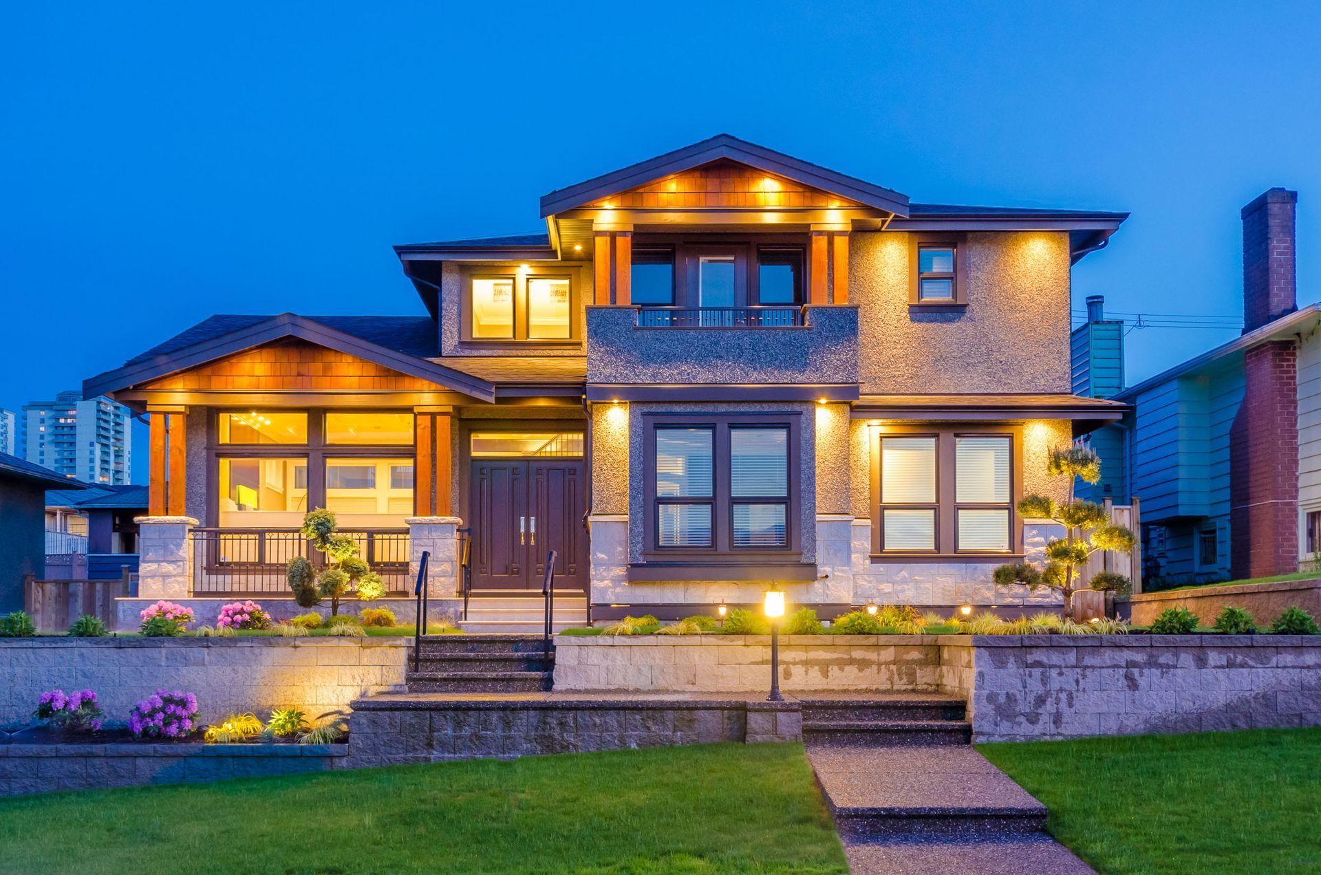 Two-story house with exterior lights, dark front doors, and a stone facade, lit up at dusk.