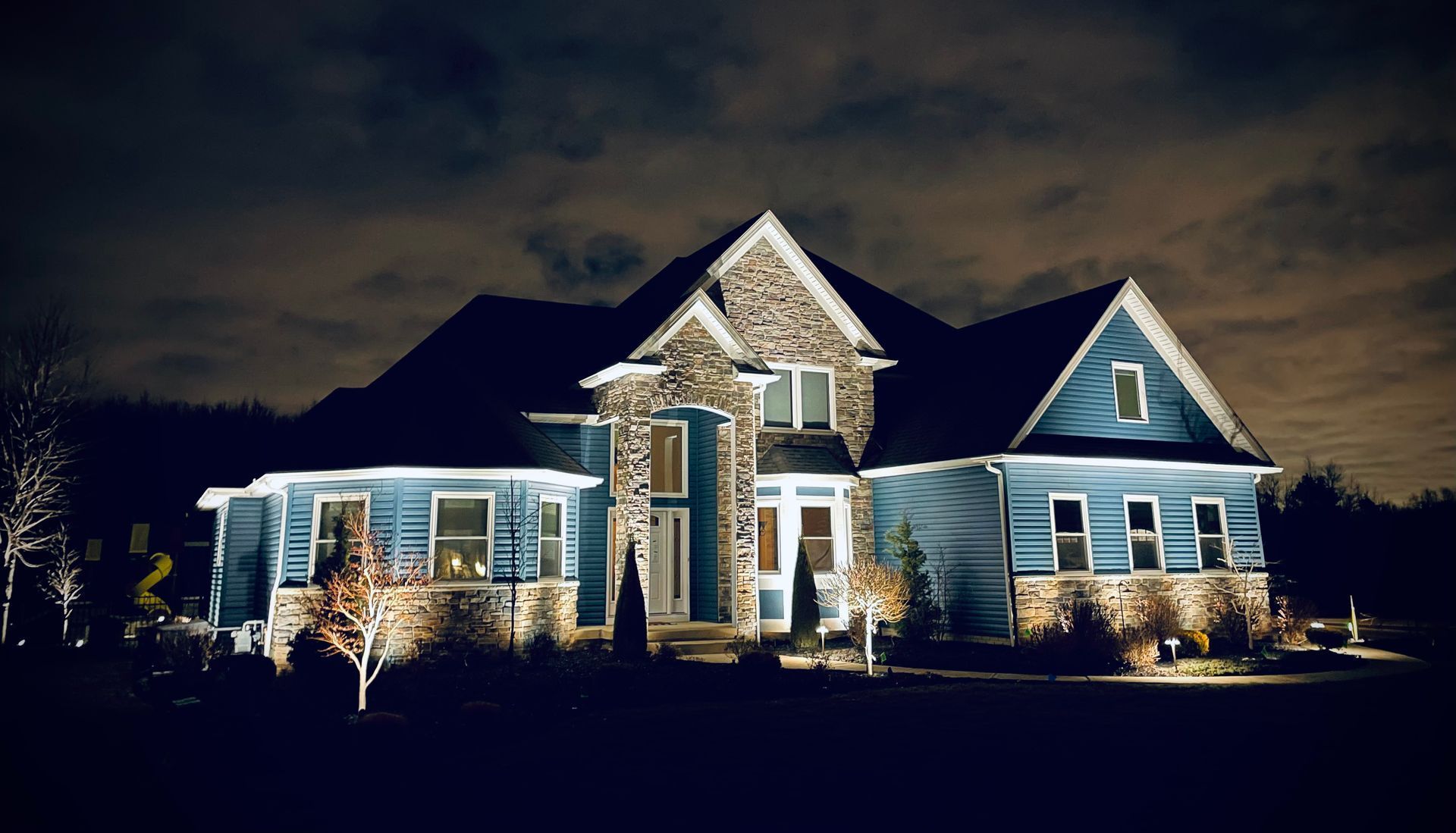 A two-story blue house with stone accents, lit up at night.