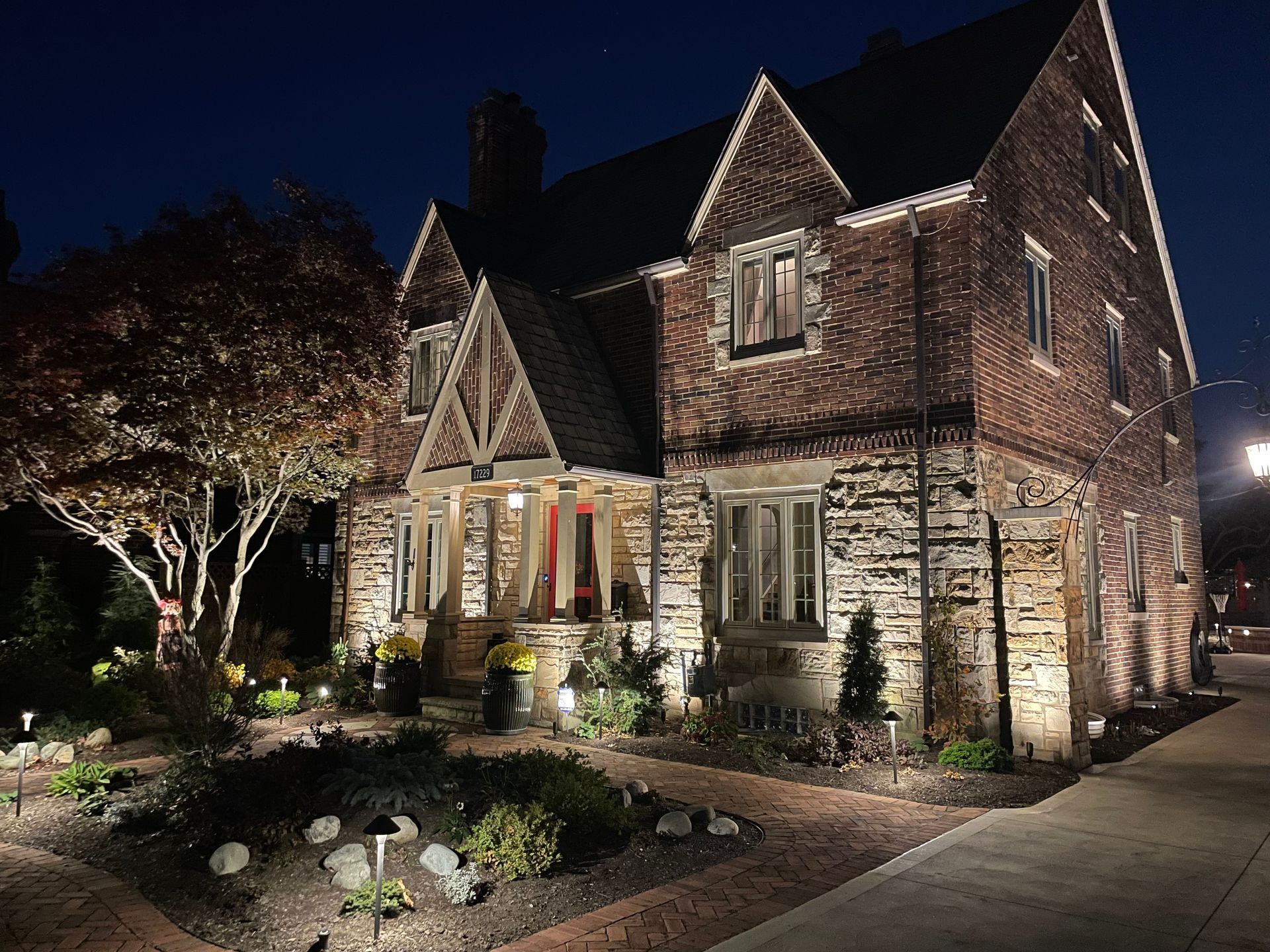 Brick house illuminated at night with garden, walkway, and tree.