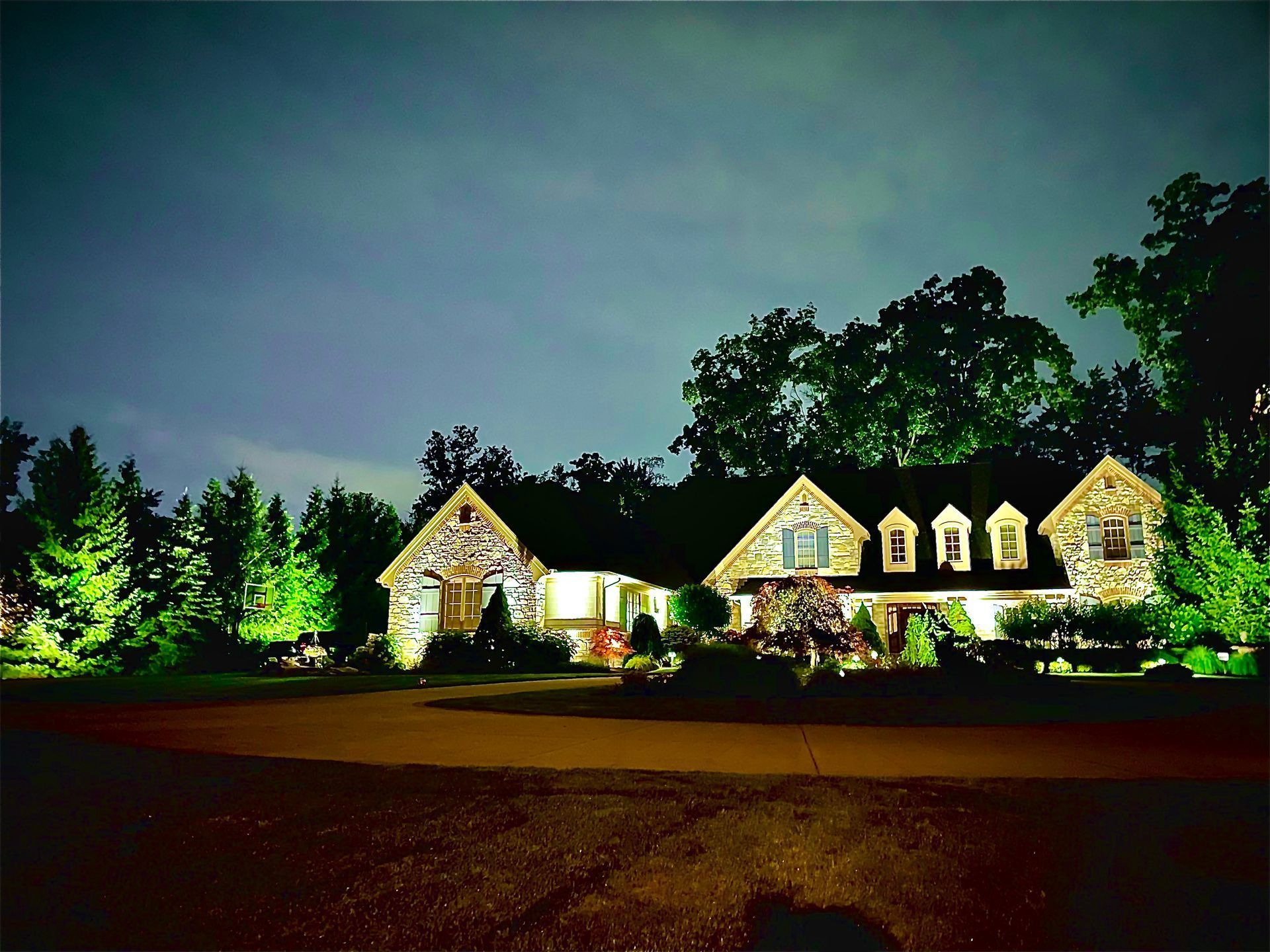 Stone house at night, lit by spotlights. Trees surround the structure, against a dark sky.