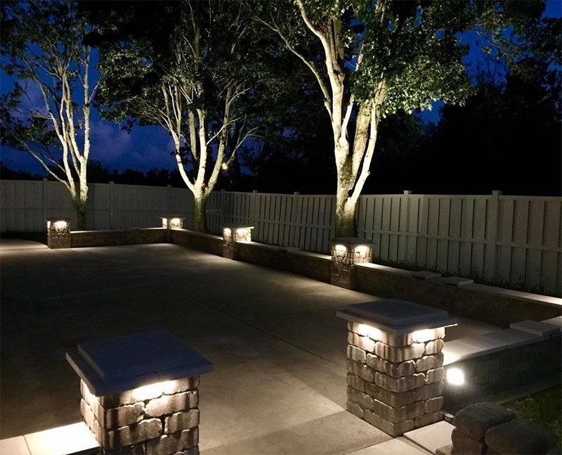Nighttime outdoor scene with trees and stone columns lit by landscape lighting.