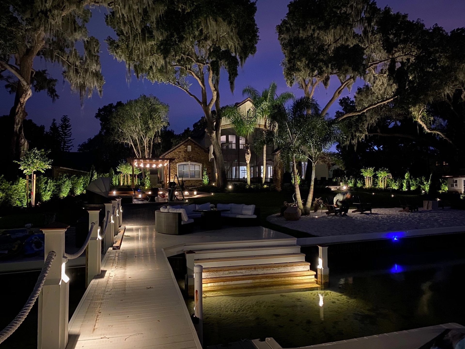 Night view of a waterfront home with illuminated dock and landscape.