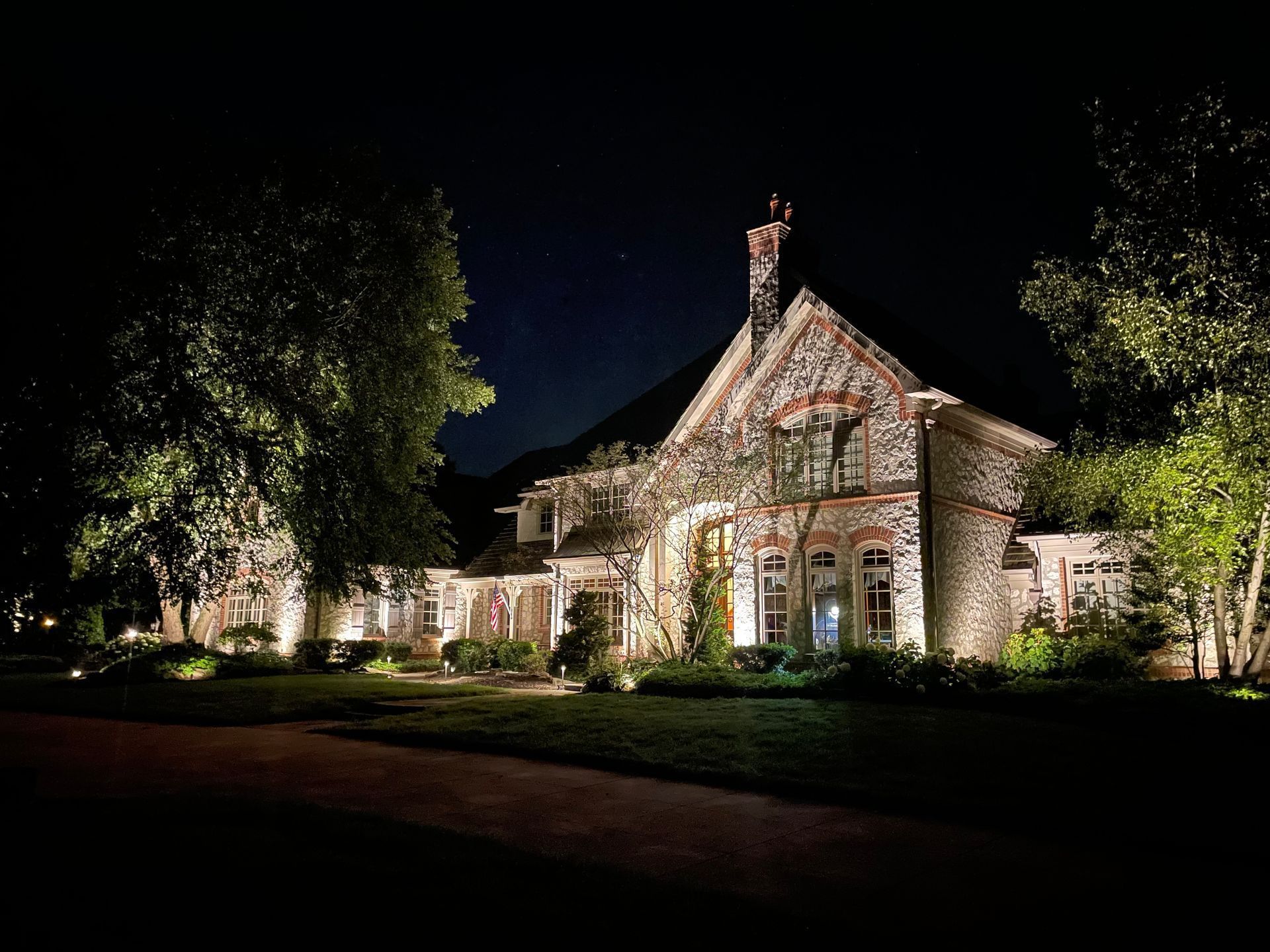 Stone house illuminated at night, flanked by trees, and a dark sky with a few visible stars.