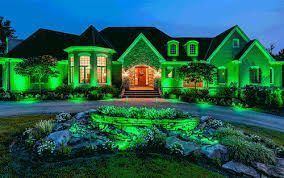 A house lit with green lights, driveway, and rock garden, at night.