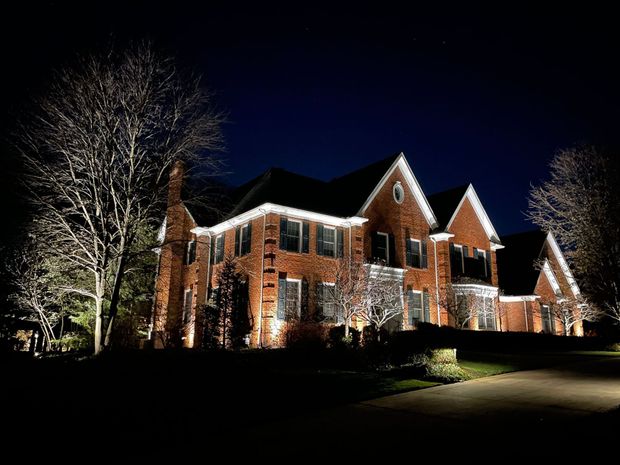 Night-lit brick house with spotlights illuminating the facade and bare trees against a dark blue sky.