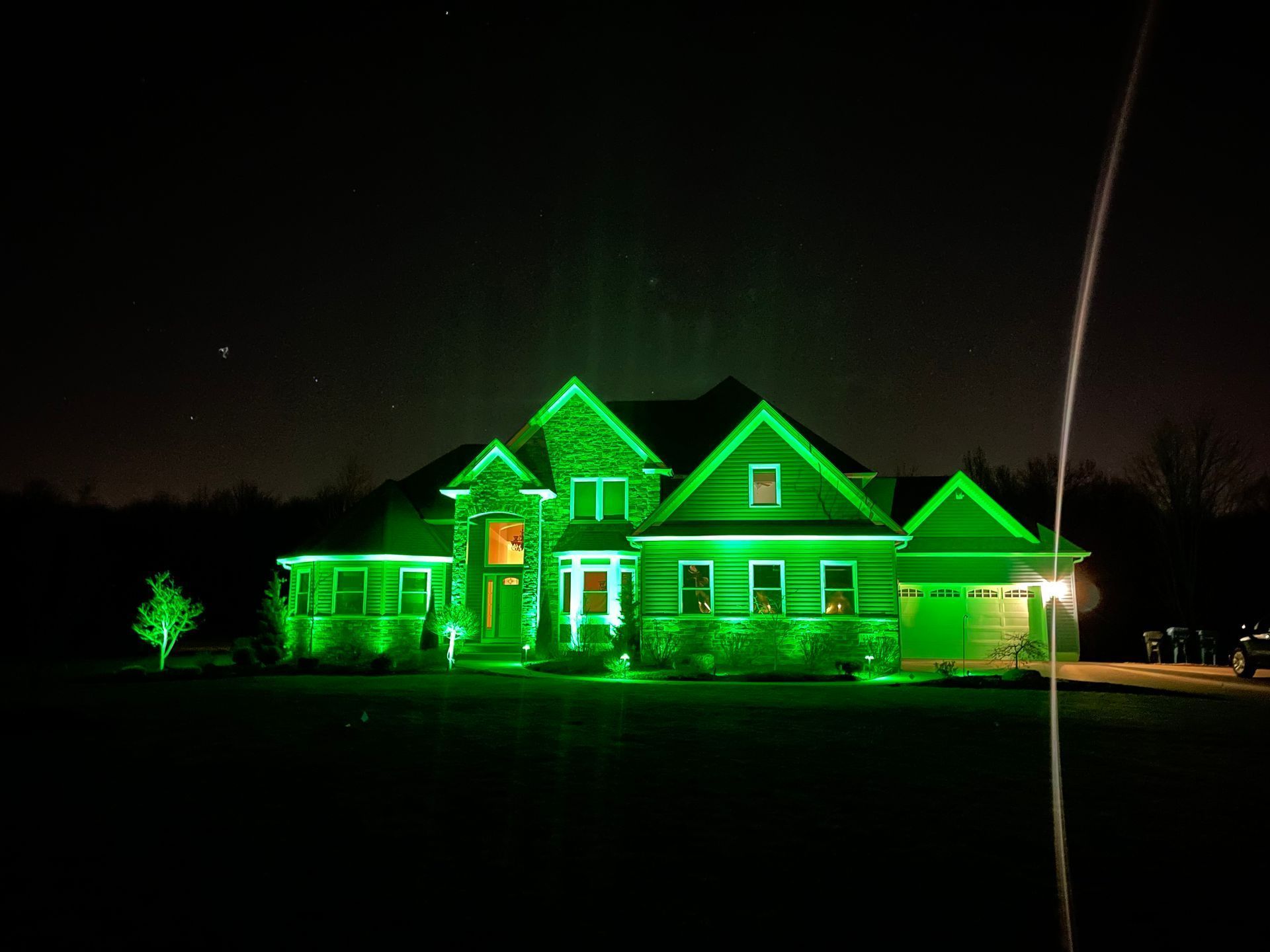 Green-lit house at night; exterior illuminated in green.