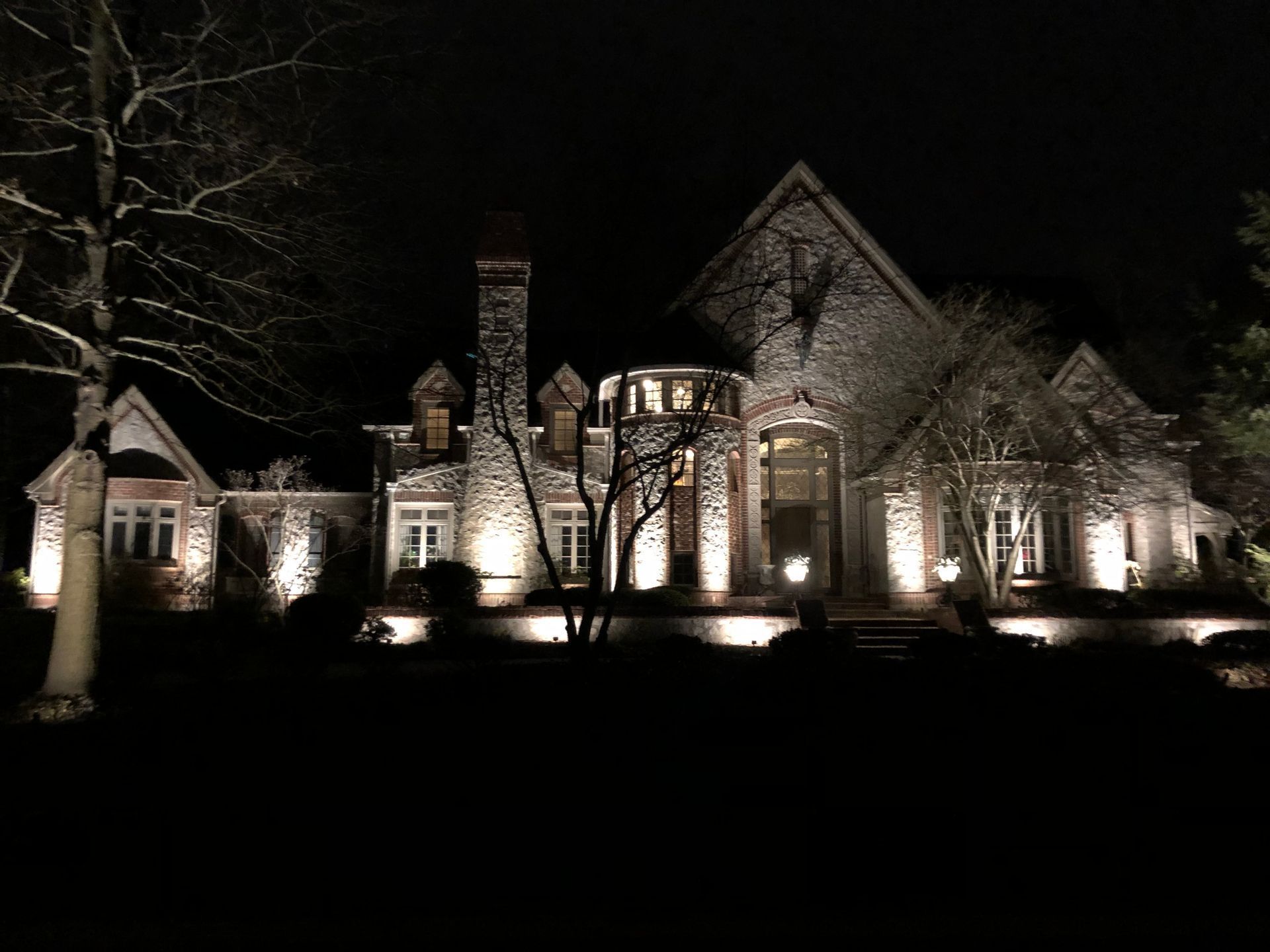 Large stone house illuminated at night by landscape lighting.
