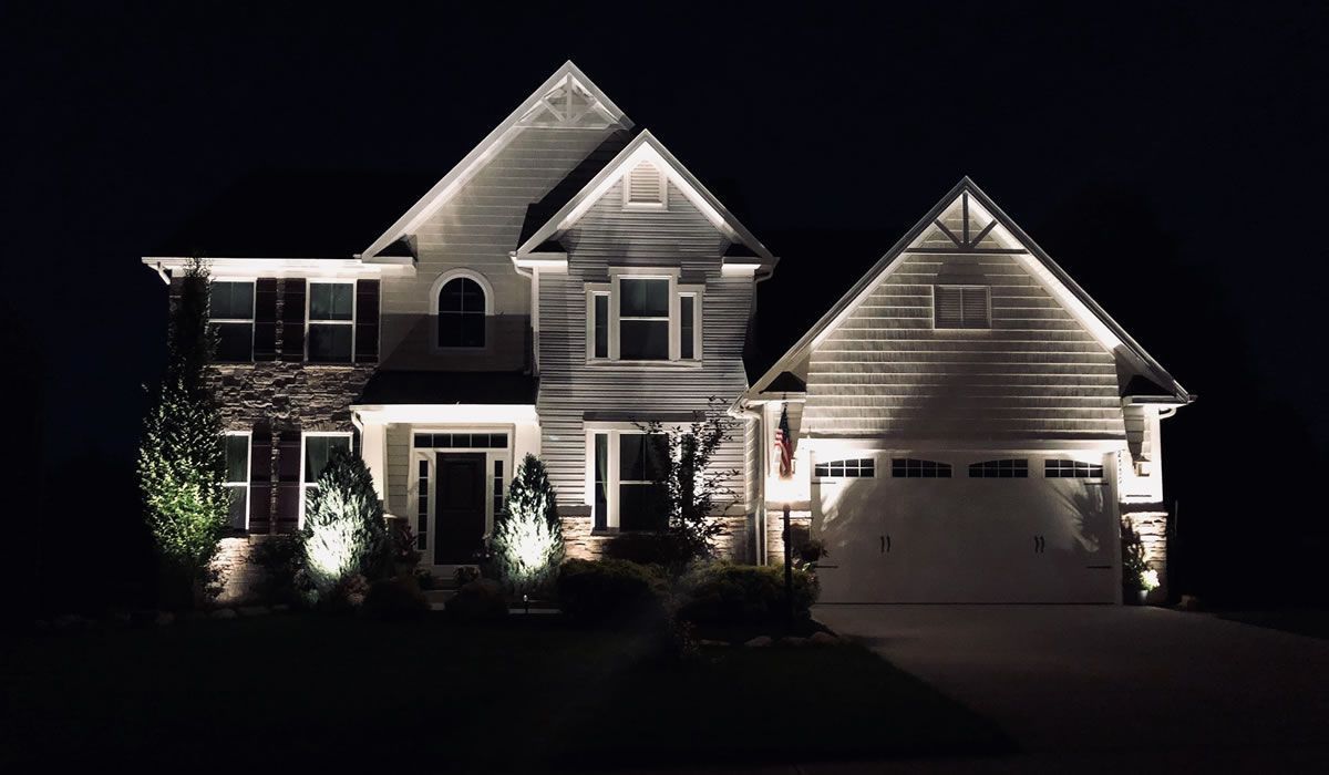 House exterior illuminated by landscape lighting at night.