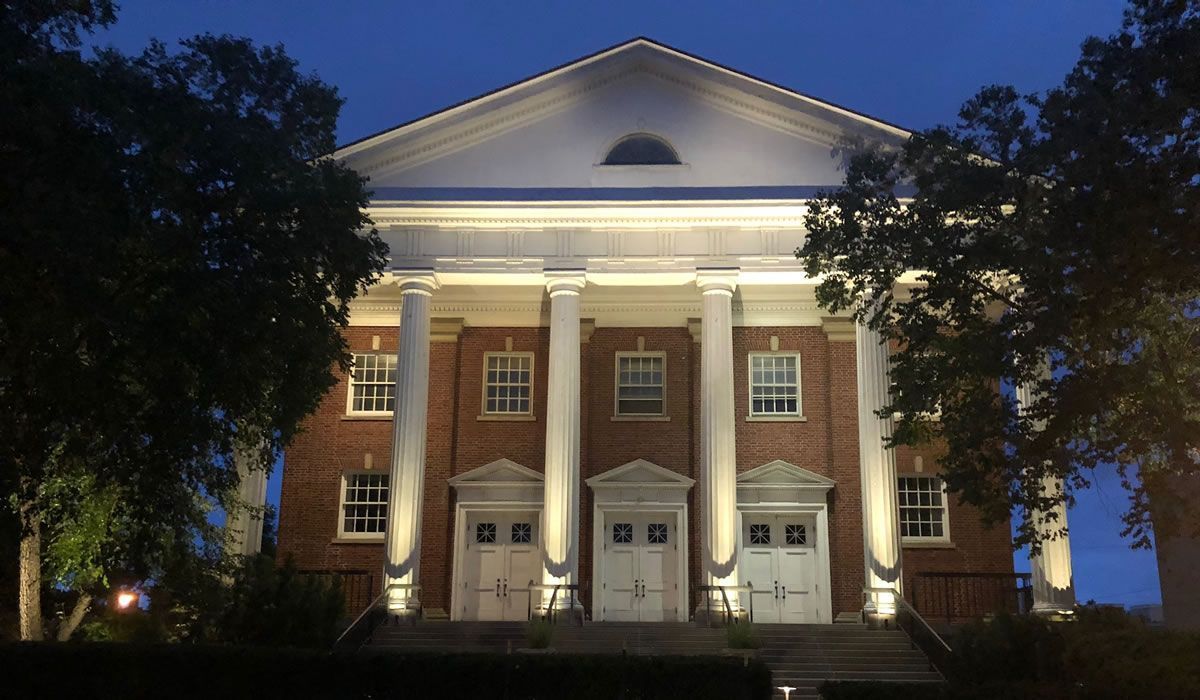 Brick building with white columns and doors illuminated at night.