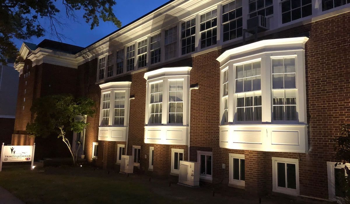 Brick building at dusk with illuminated bay windows and bright white trim.