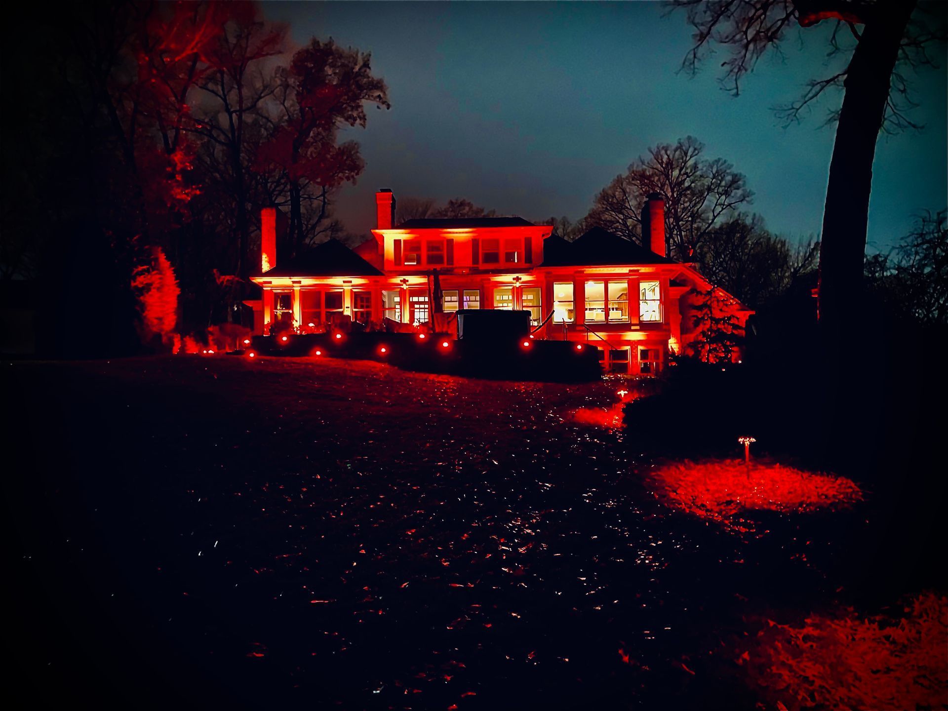 House illuminated in red at night, trees surrounding.