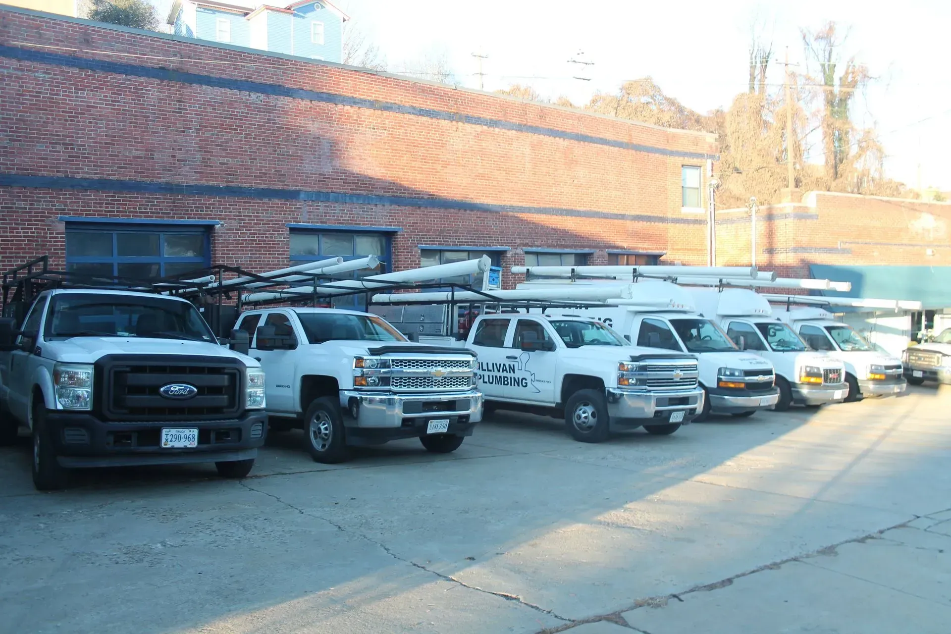 A row of white work trucks parked in front of a brick building.