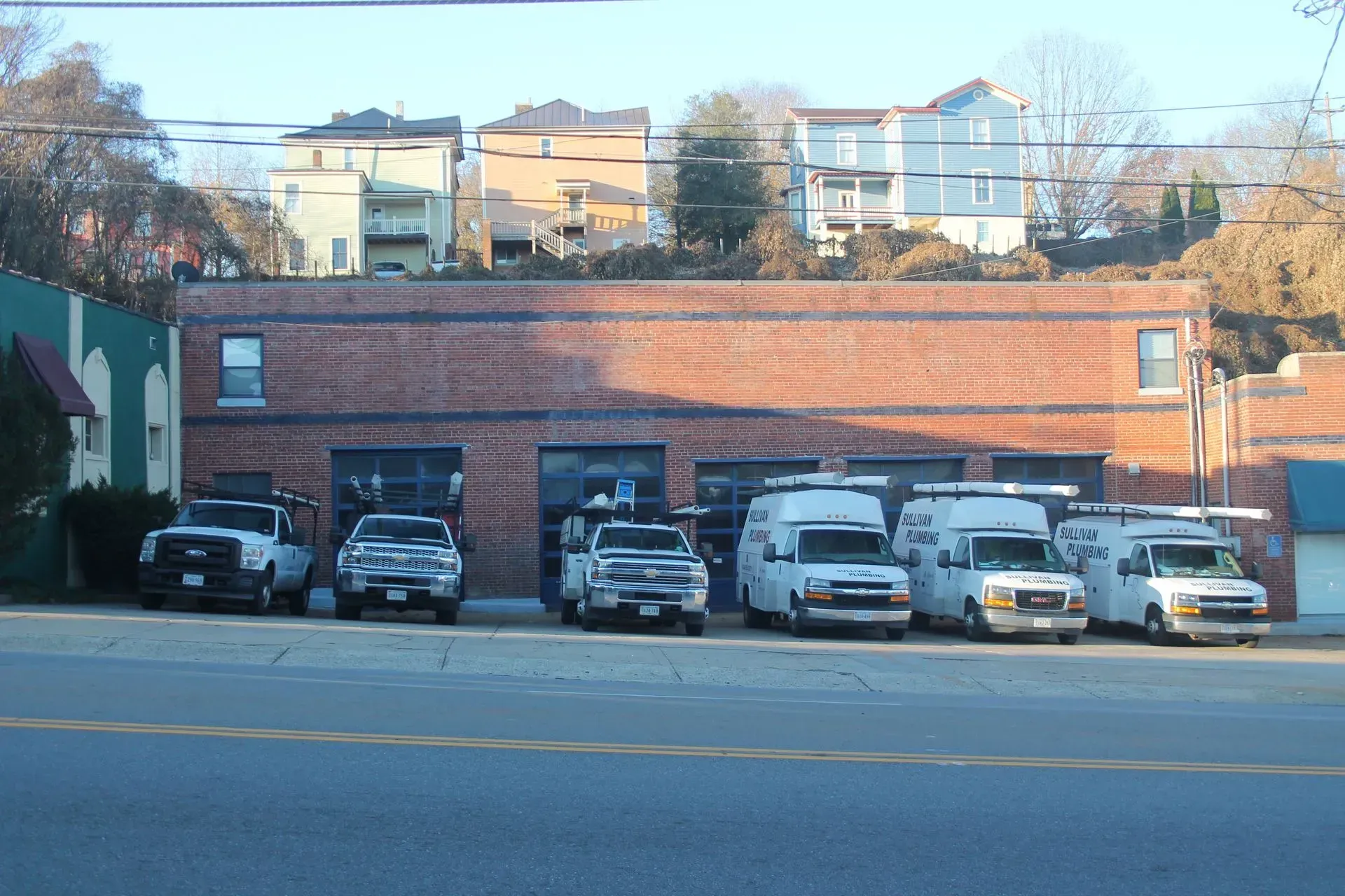Brick building with open garage doors and several service trucks parked out front.