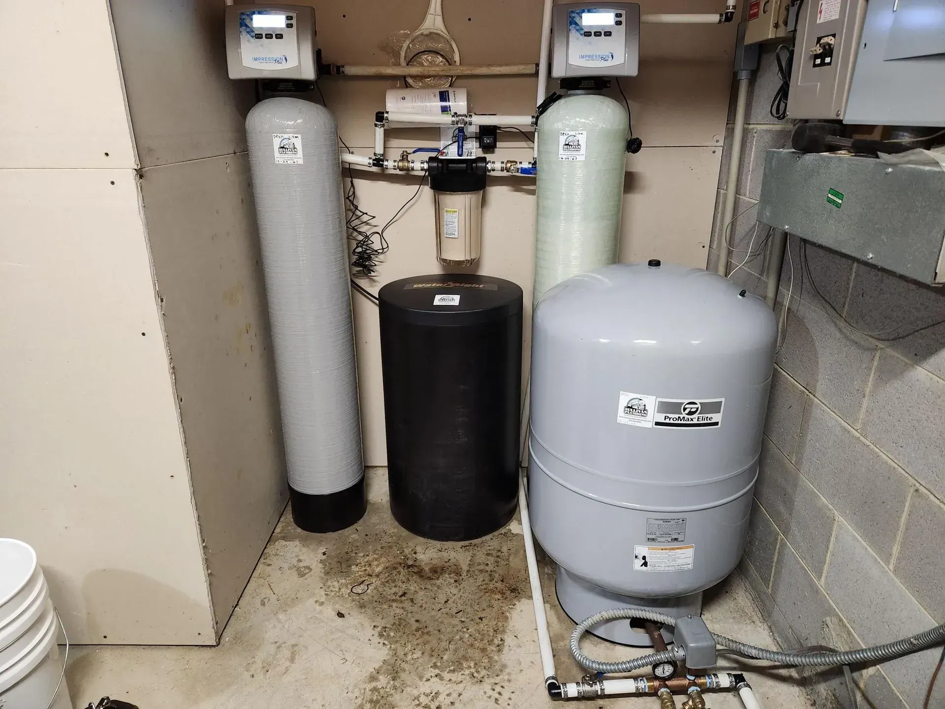 Water filtration and treatment system in a basement.  Tanks, gauges, and a pressure tank are visible.