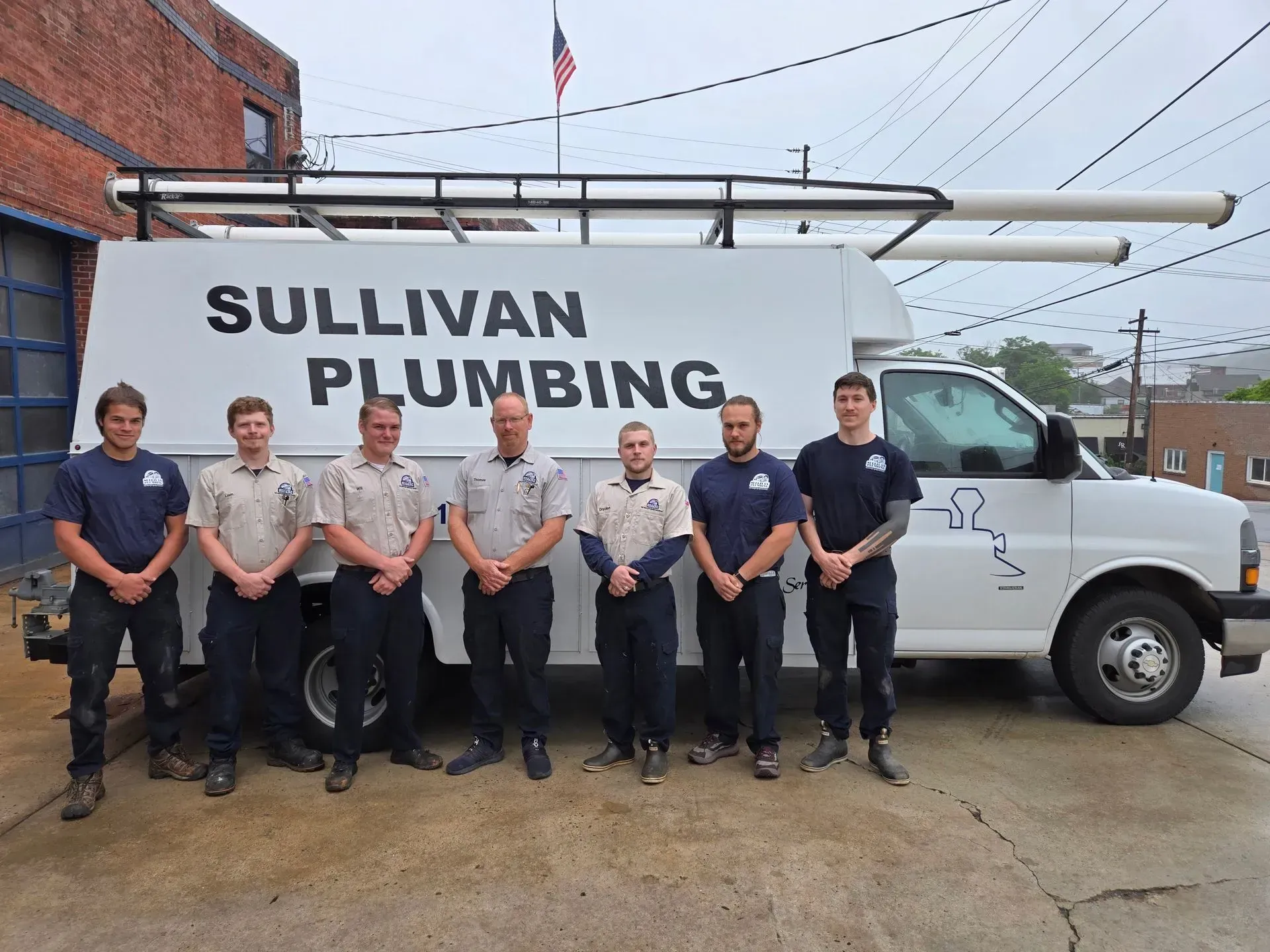 Team of plumbers in uniforms pose in front of a Sullivan Plumbing van.