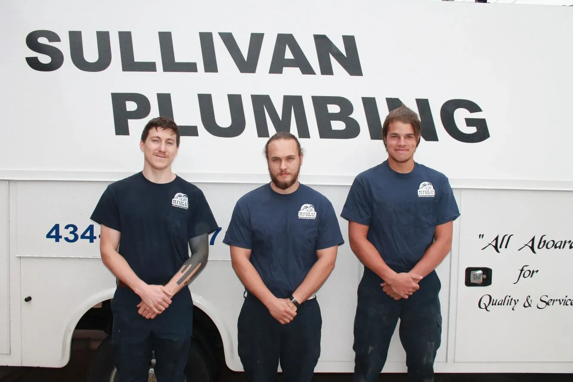 Three plumbers in blue shirts pose in front of a Sullivan Plumbing truck.