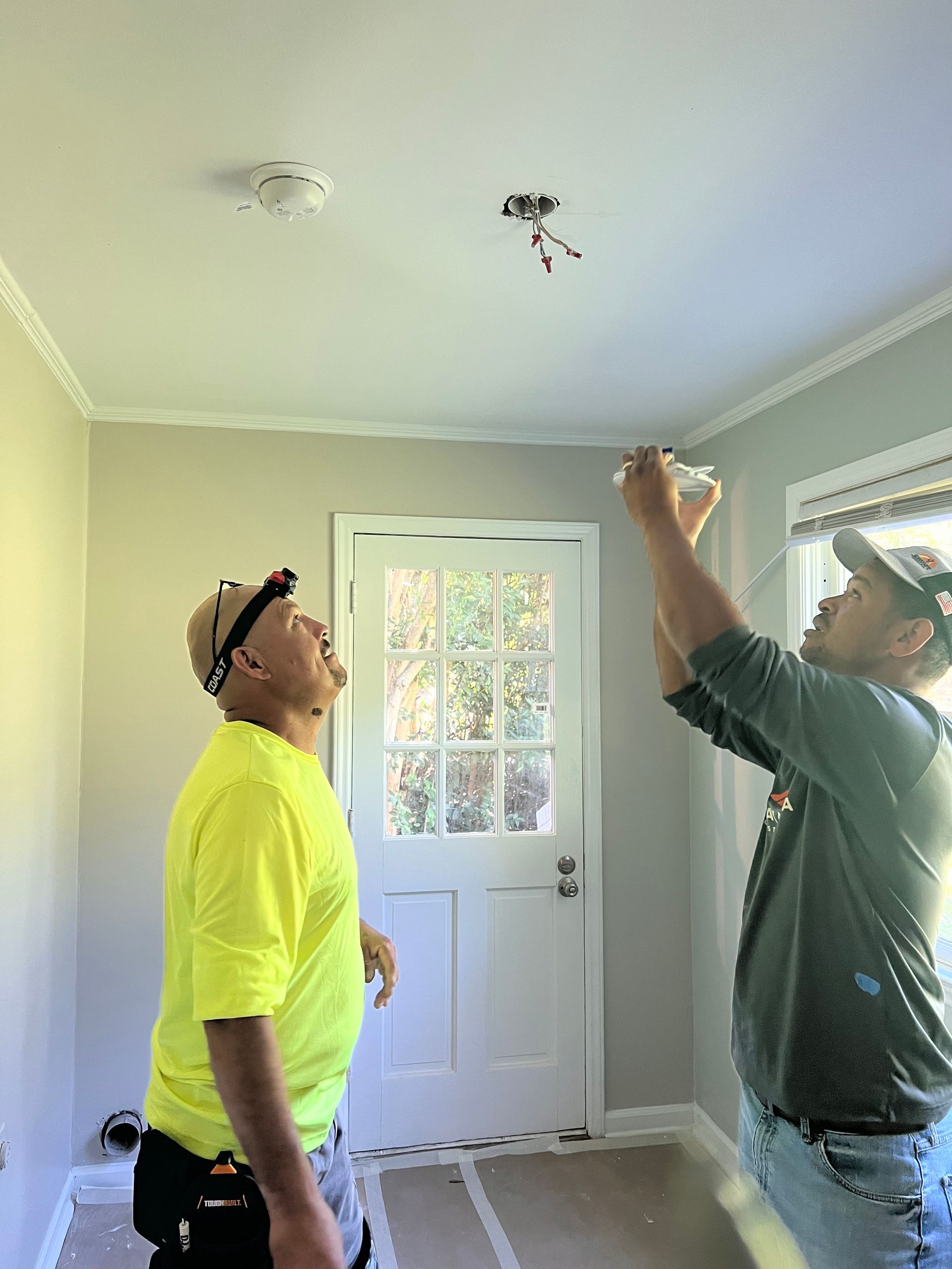 Two men are working on a ceiling light in a room.