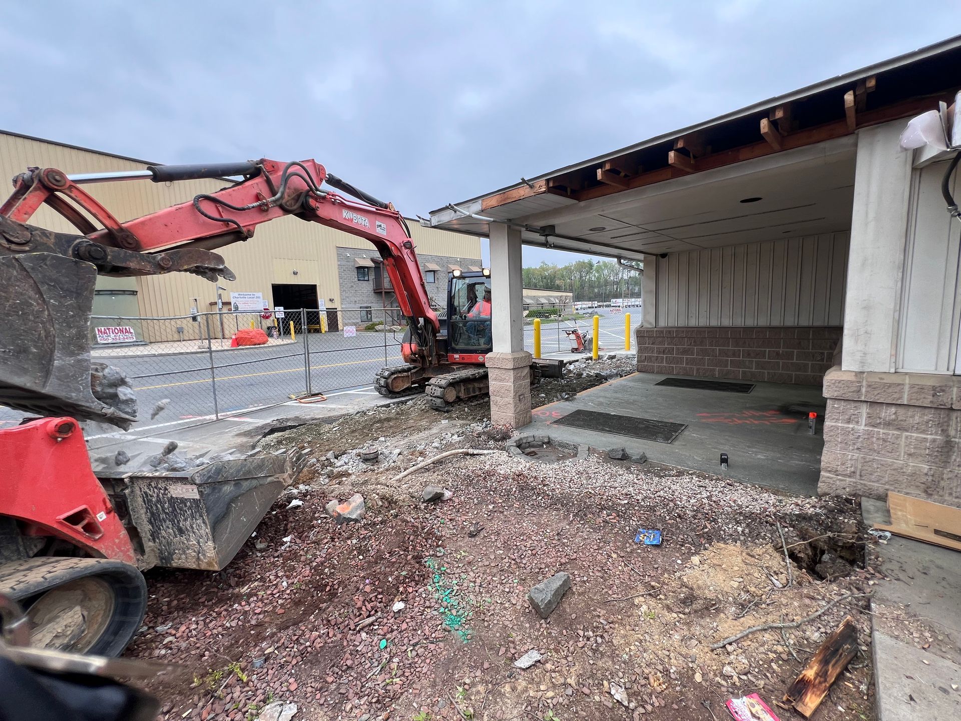 A red excavator is moving dirt in front of a building.