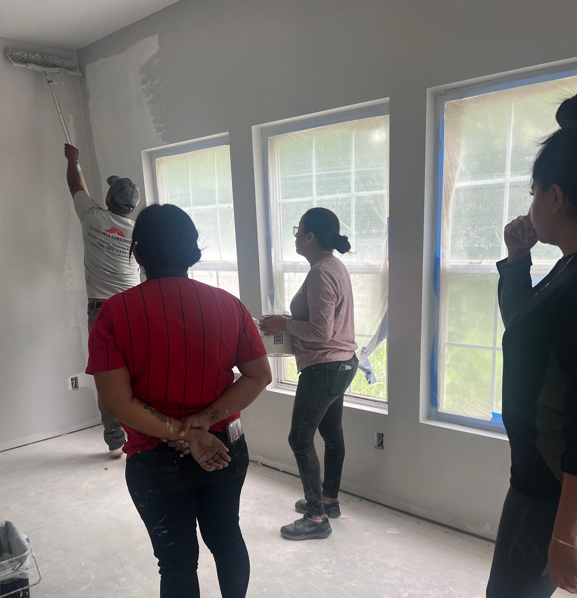 A group of people are standing in a room with a man painting a wall.