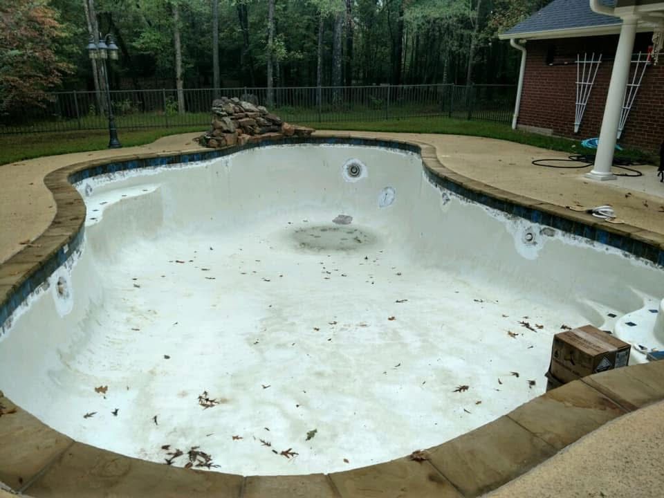 An empty swimming pool in a backyard with a fence around it.