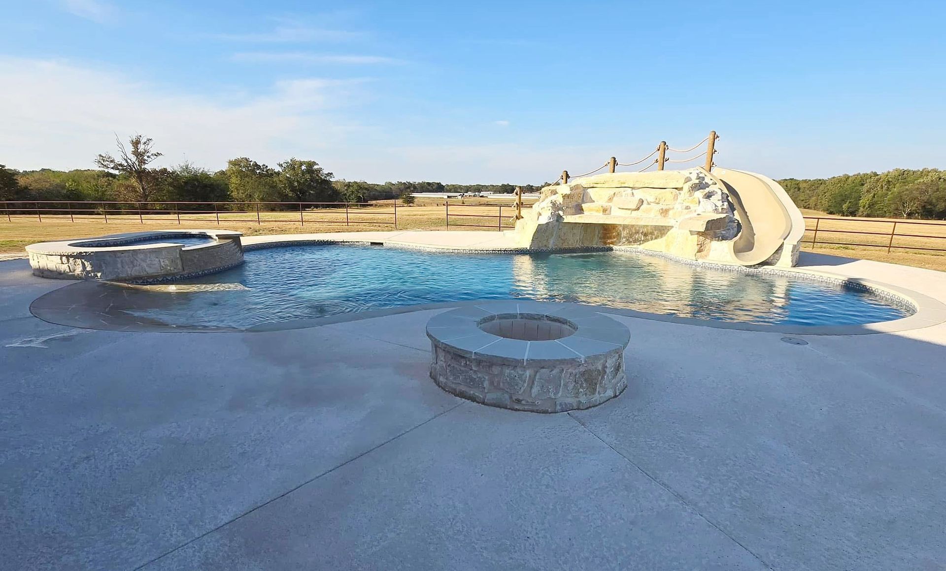 A large swimming pool with a slide and a fire pit.
