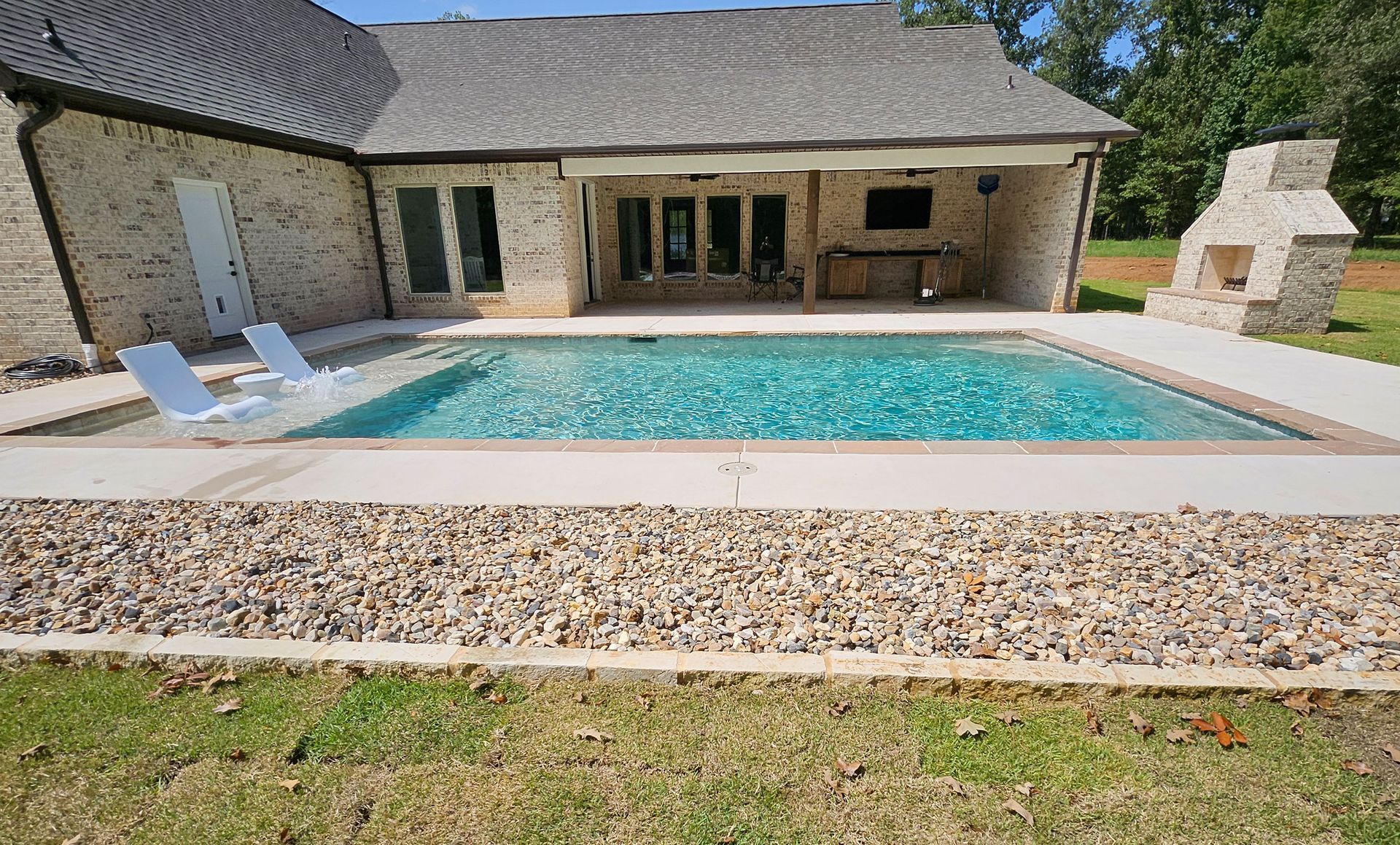 A large swimming pool in front of a brick house.