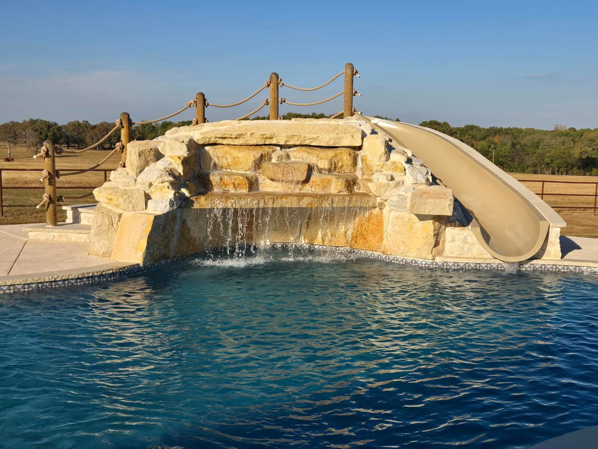 A large swimming pool with a waterfall and a slide.
