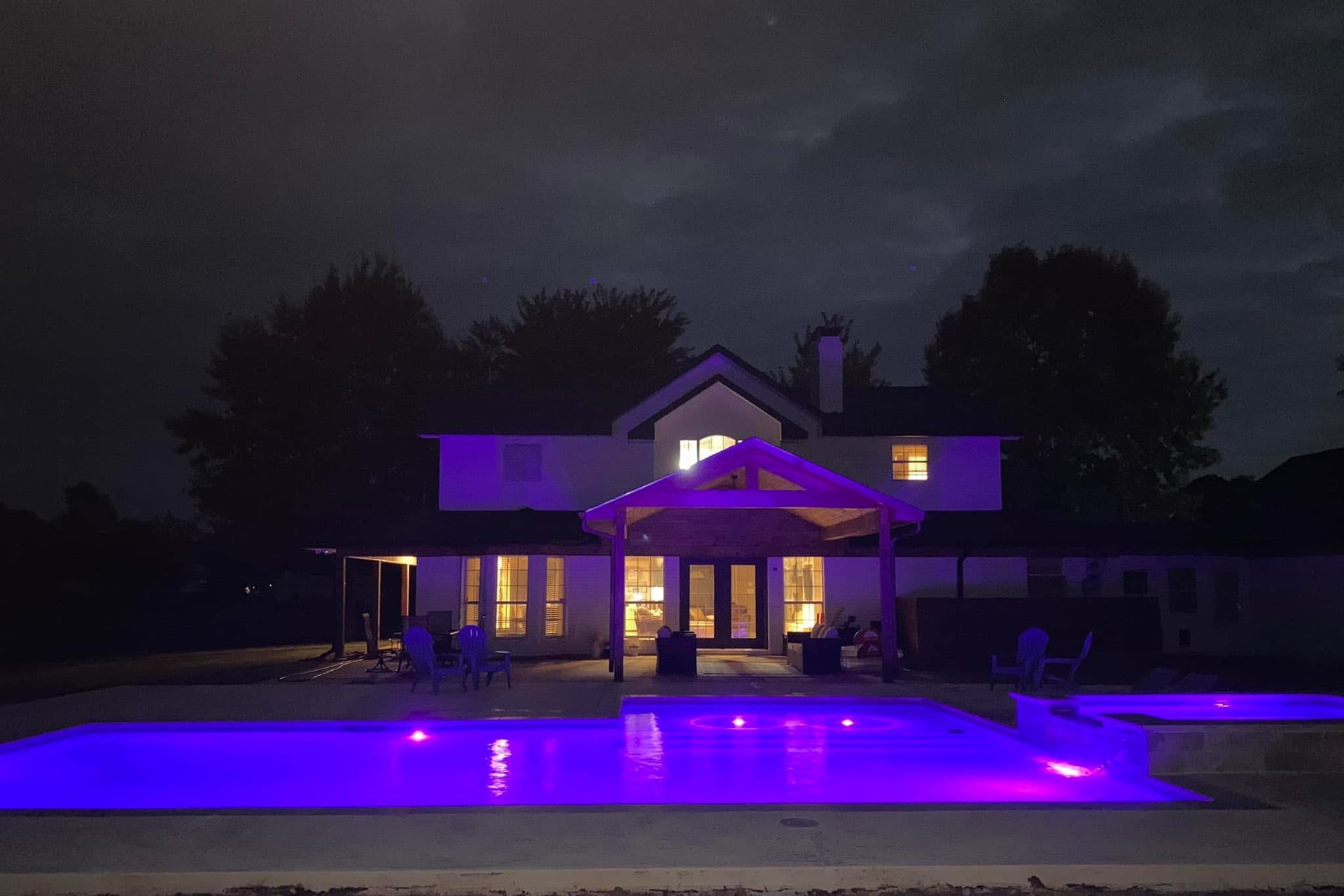A large swimming pool is lit up at night with purple lights.
