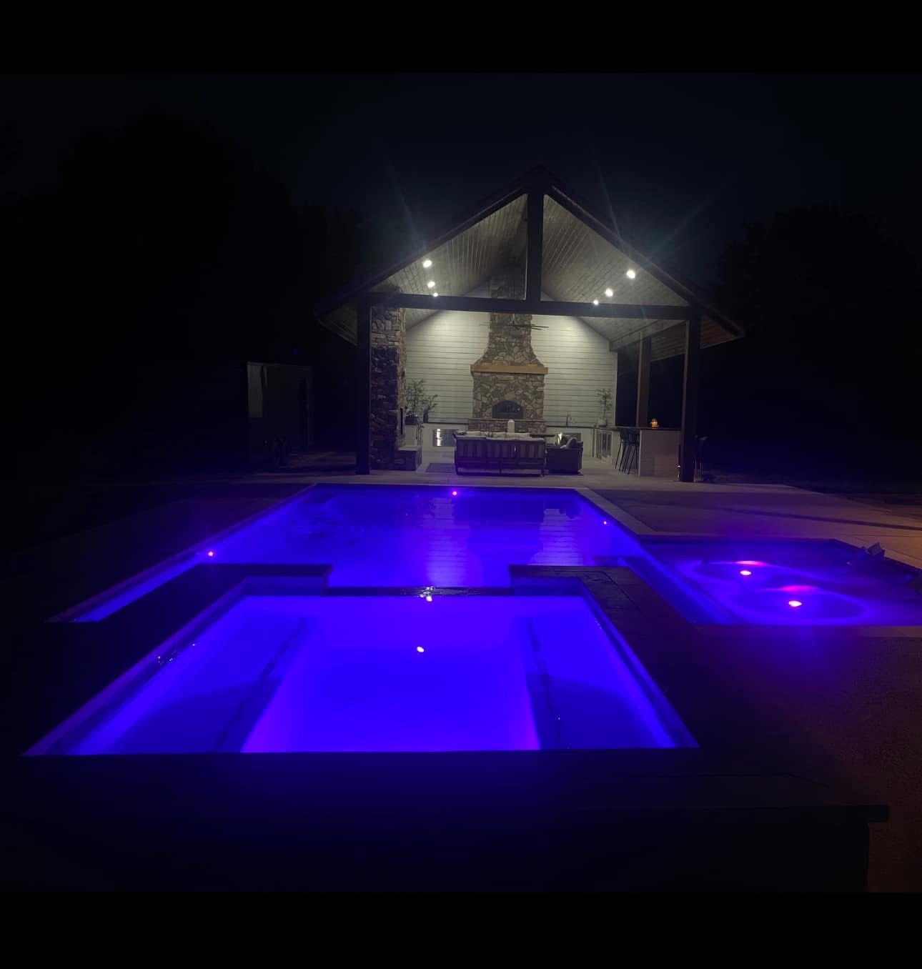 A large swimming pool is lit up at night with purple lights.