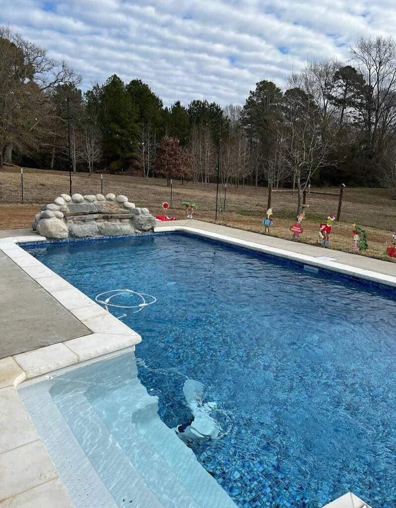 A large swimming pool with a waterfall in the backyard.