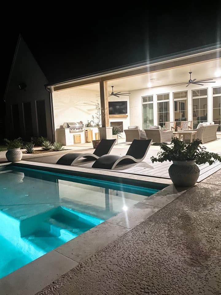 A large swimming pool is lit up at night in front of a house.