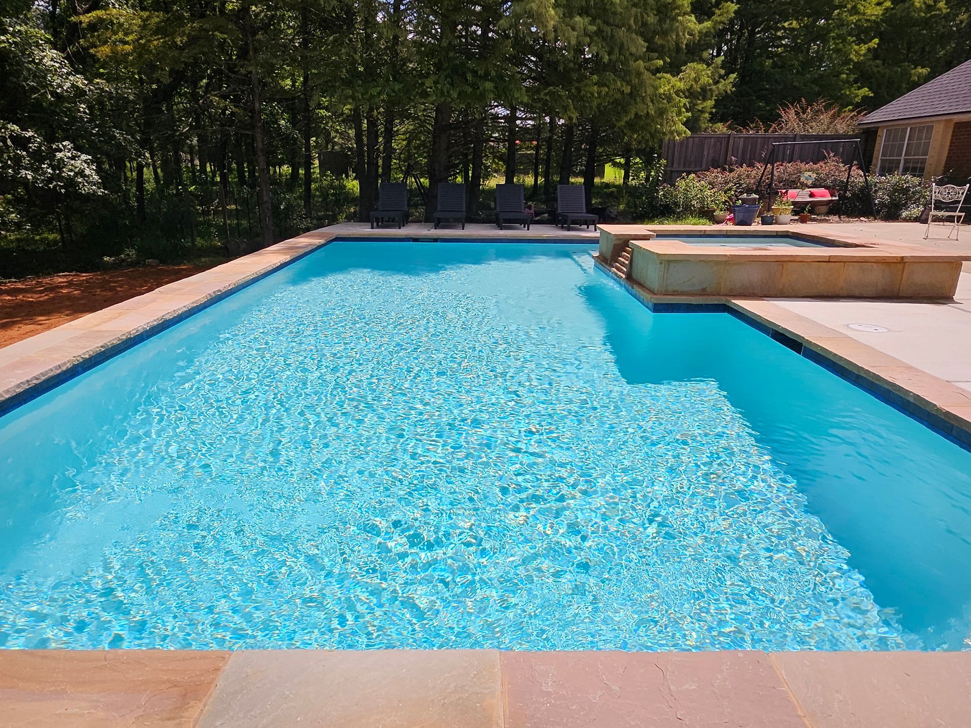 A large swimming pool is surrounded by trees and a patio.