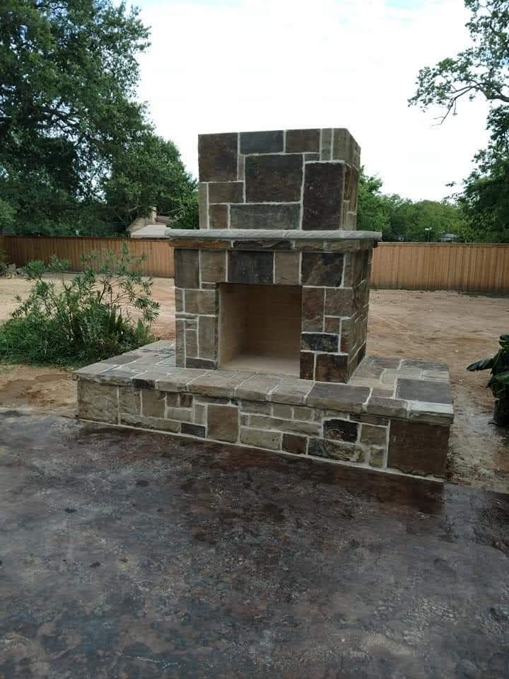 A stone fireplace in a backyard with a wooden fence in the background.